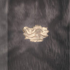 A compact Clérachic pendant with a frilled, cream-toned shade, lit against a dark wall dappled with shadow.