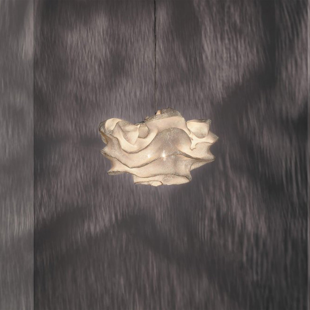 A compact Clérachic pendant with a frilled, cream-toned shade, lit against a dark wall dappled with shadow.