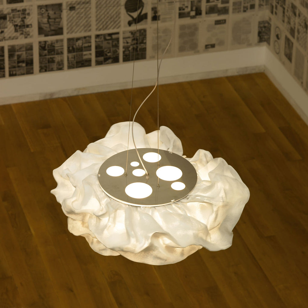 Seen from above, a Clérachic pendant rests on a timber floor, its frilled white shade around a round plate with circular cut-outs.