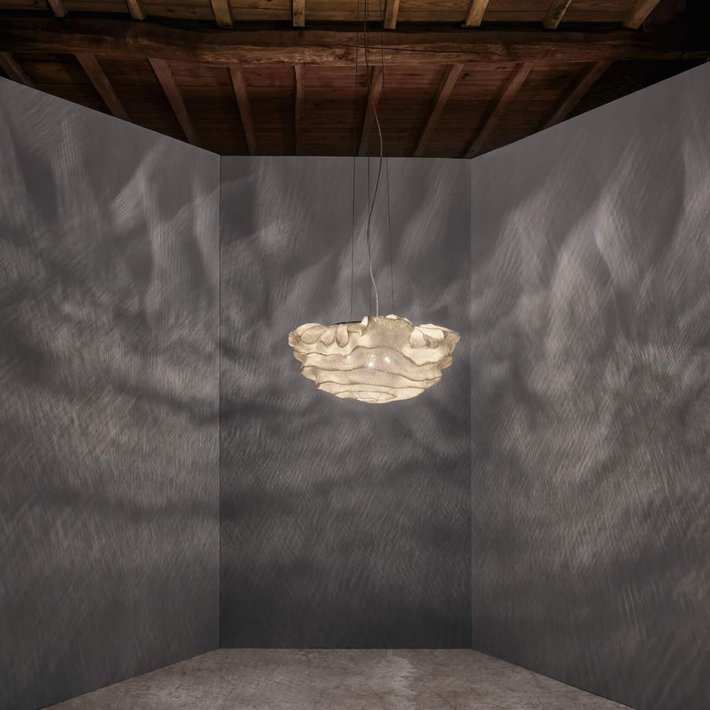 A small Clérachic pendant glowing in the middle of a dark grey room with a rough timber ceiling and a concrete floor.
