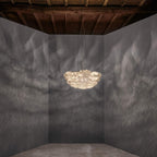 A small Clérachic pendant glowing in the middle of a dark grey room with a rough timber ceiling and a concrete floor.