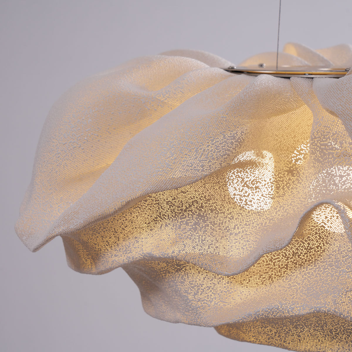 Close view of the frilled edge and perforated mesh of this Clérachic pendant, lit warm in a bright room.