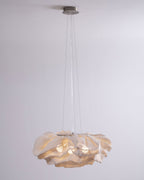 A Clérachic pendant hangs from a round ceiling plate on fine wires, its ruffled shade glowing against a pale grey wall.