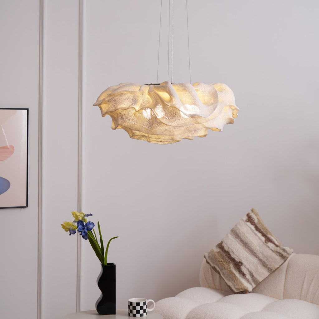 A lit Clérachic pendant above a pale sofa with a striped cushion, with irises in a black vase and a framed print on the wall.