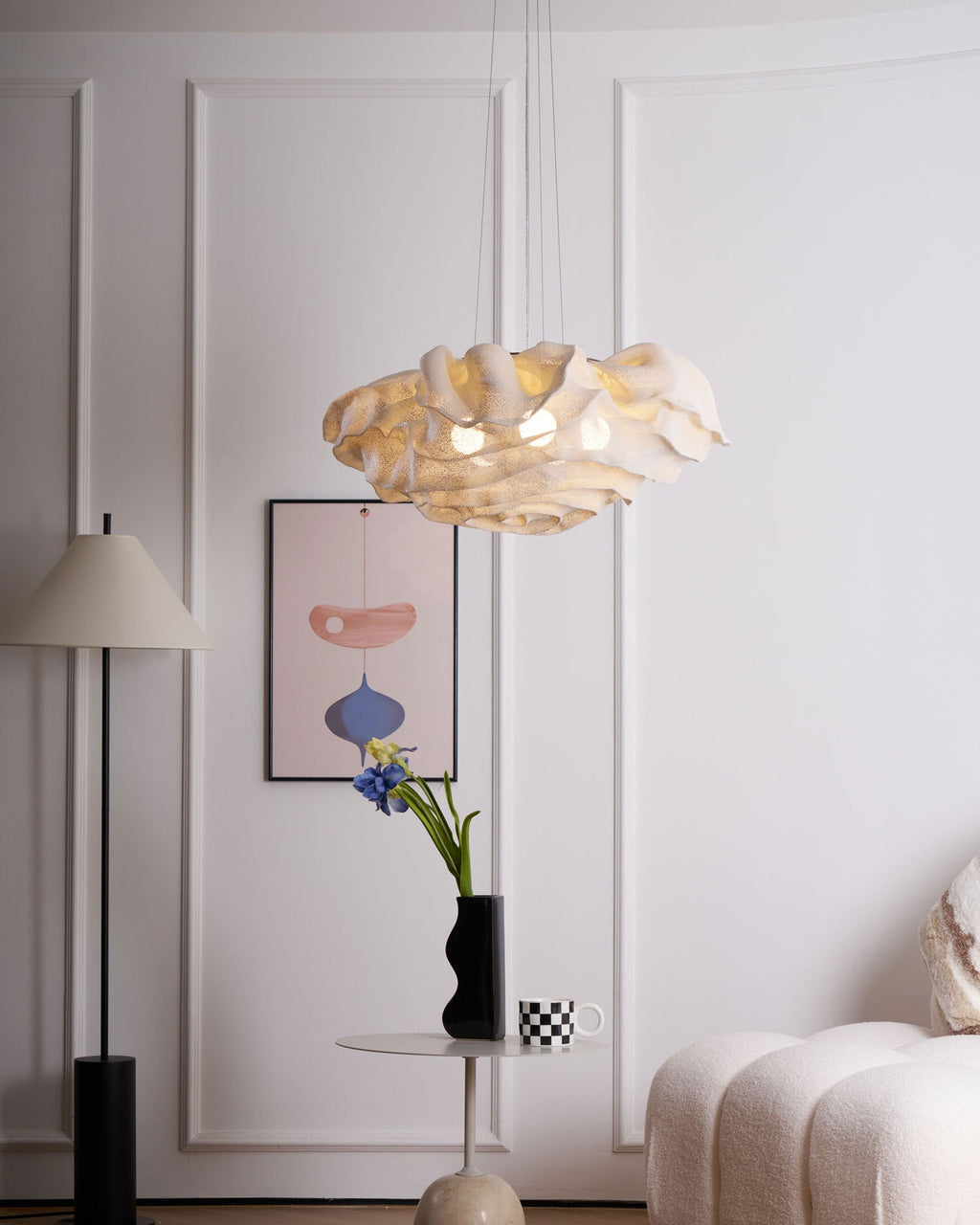 Beside a white panelled wall and a standing lamp, a Clérachic pendant hangs above a cream sofa and a small round table.