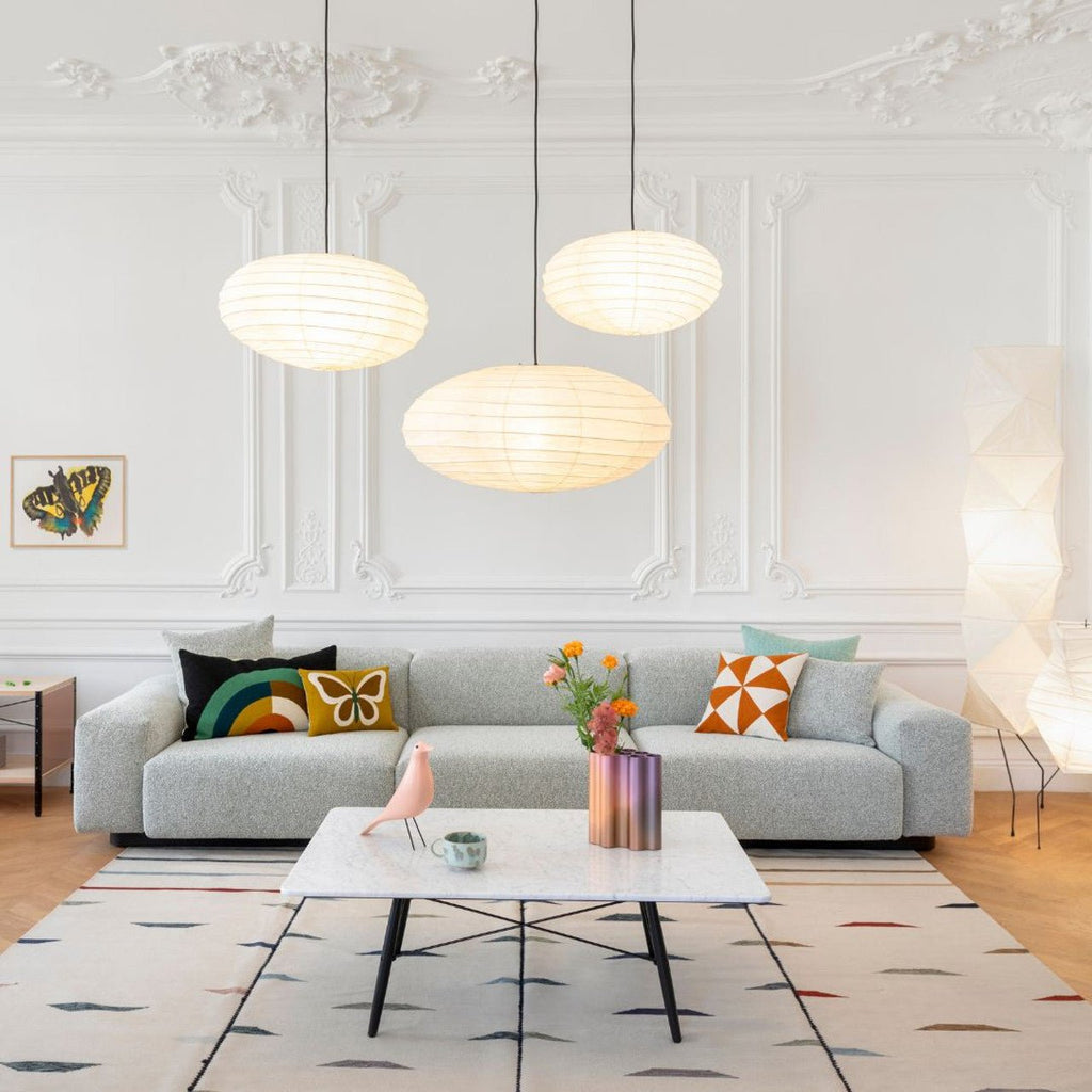 Clérachic oval paper pendant light hung as a lit trio at staggered heights above a grey sofa in a panelled, moulded living room.