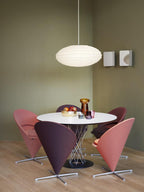 Clérachic oval paper pendant light hung low over a round white dining table ringed with pink and burgundy cone chairs.
