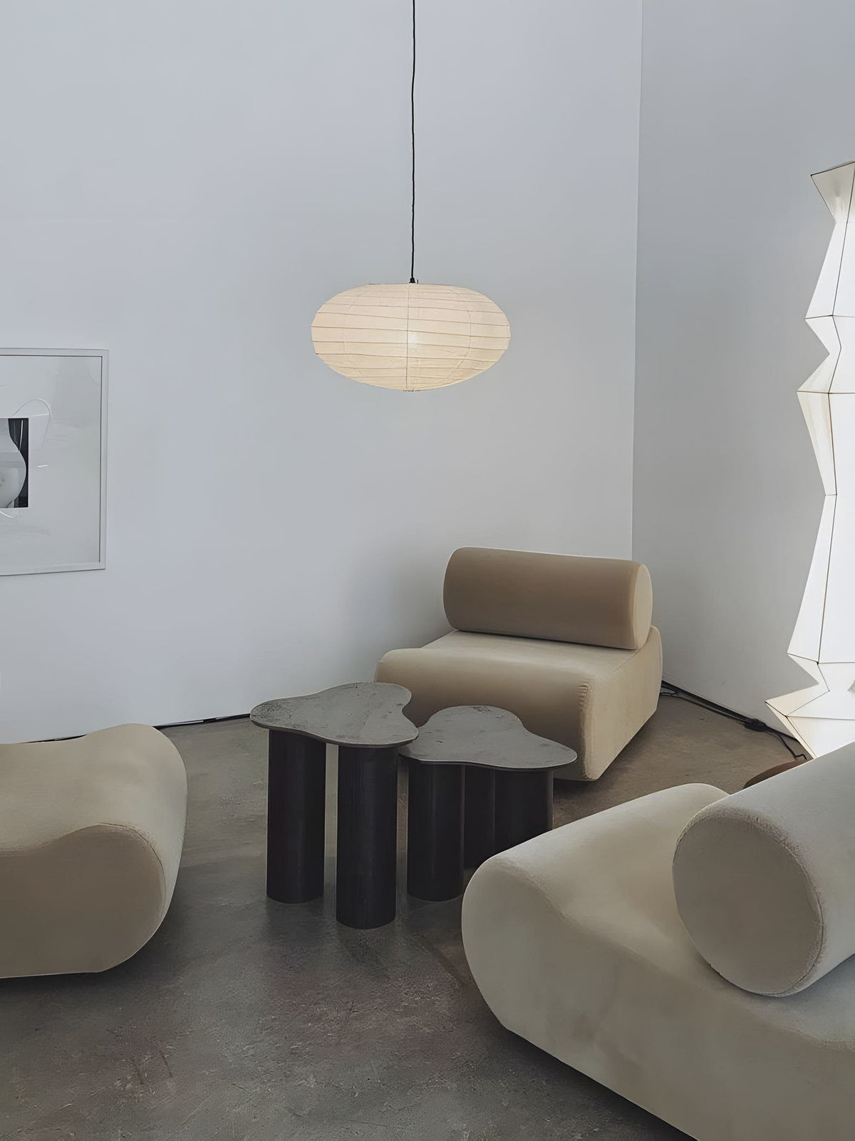 Clérachic oval paper pendant light lit in the same white room from further back, both lounge chairs and the concrete floor in shot.