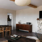 Clérachic oval paper pendant light cropped at the top of the frame beside an exposed timber beam, a kitchen doorway visible beyond the living room.