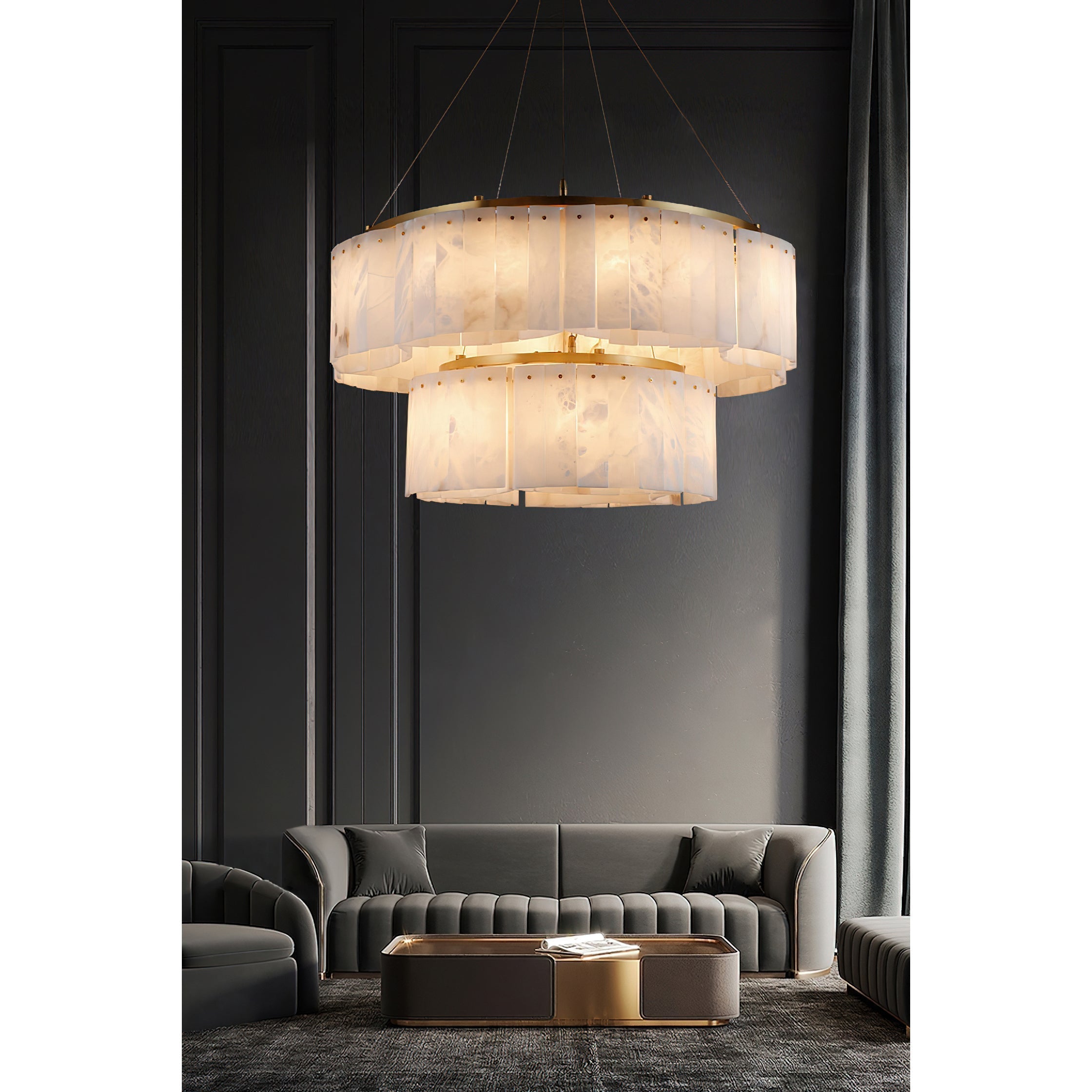 The two-tier Clérachic Willamette Alabaster Drum Chandelier lighting a panelled salon above grey velvet sofas.