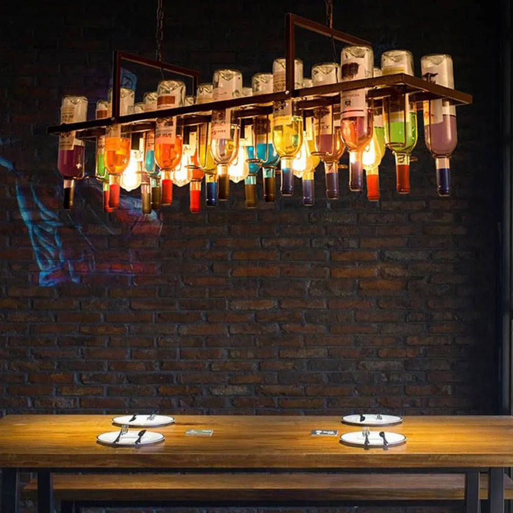 Clérachic Wine Bottle Glass Pendant Light hangs over a wooden dining table against a dark brick wall.