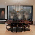 A Clérachic mesh chandelier hung above a dark wooden dining table and chairs, in front of a large window onto a stone wall.