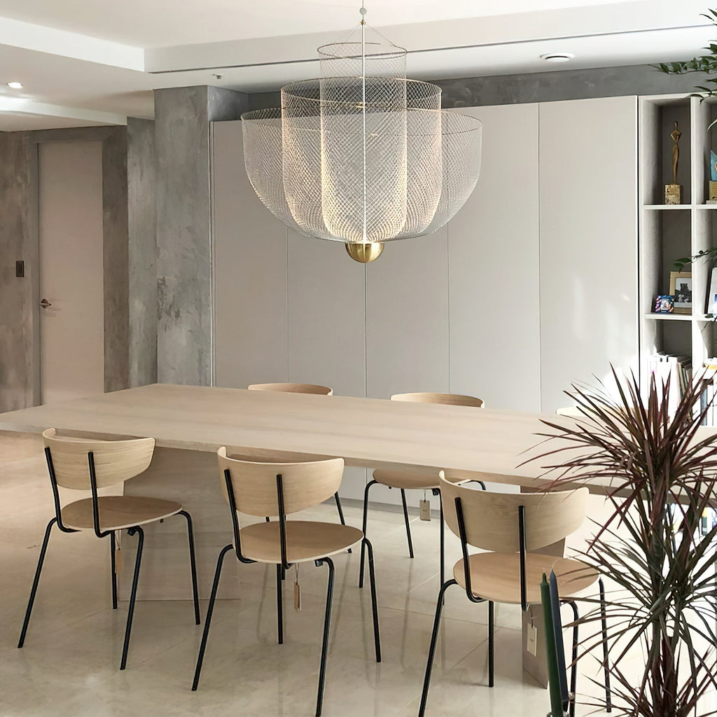 This Clérachic wire-mesh chandelier lights a long pale wood table with wooden chairs, in front of a concrete pillar and white cabinets.