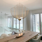 Clérachic mesh chandelier above a rough-sawn timber table with candles, with white curtains and shuttered windows behind.