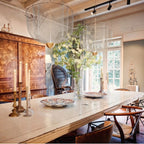 Clérachic wire-mesh chandelier in a room with a white-painted table of flowers and candles, an arched-back chair and a bright window.