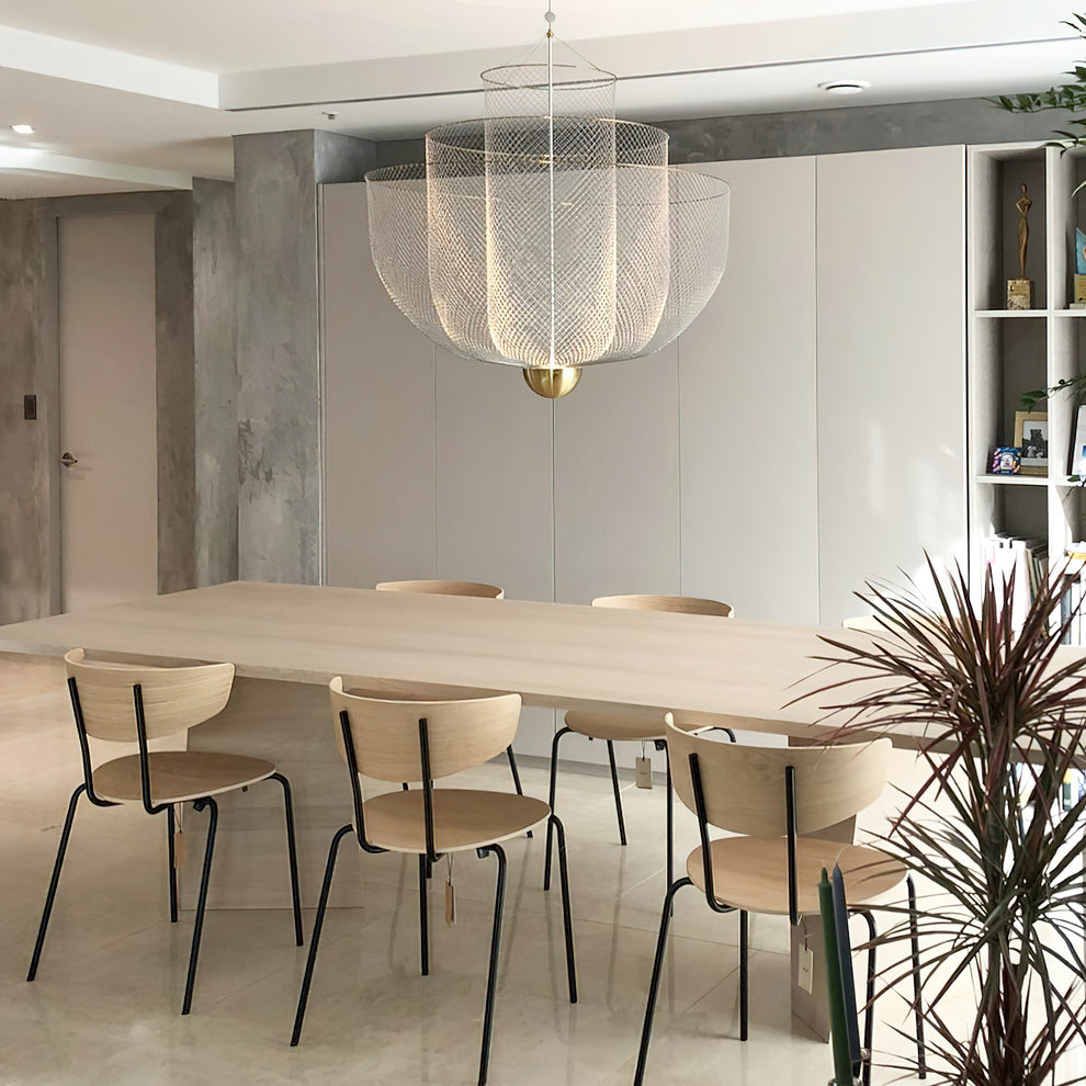 A Clérachic mesh chandelier over a long pale wood table with slim chairs, beside a spiky houseplant and a concrete column.