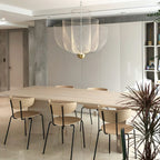 A Clérachic mesh chandelier over a long pale wood table with slim chairs, beside a spiky houseplant and a concrete column.