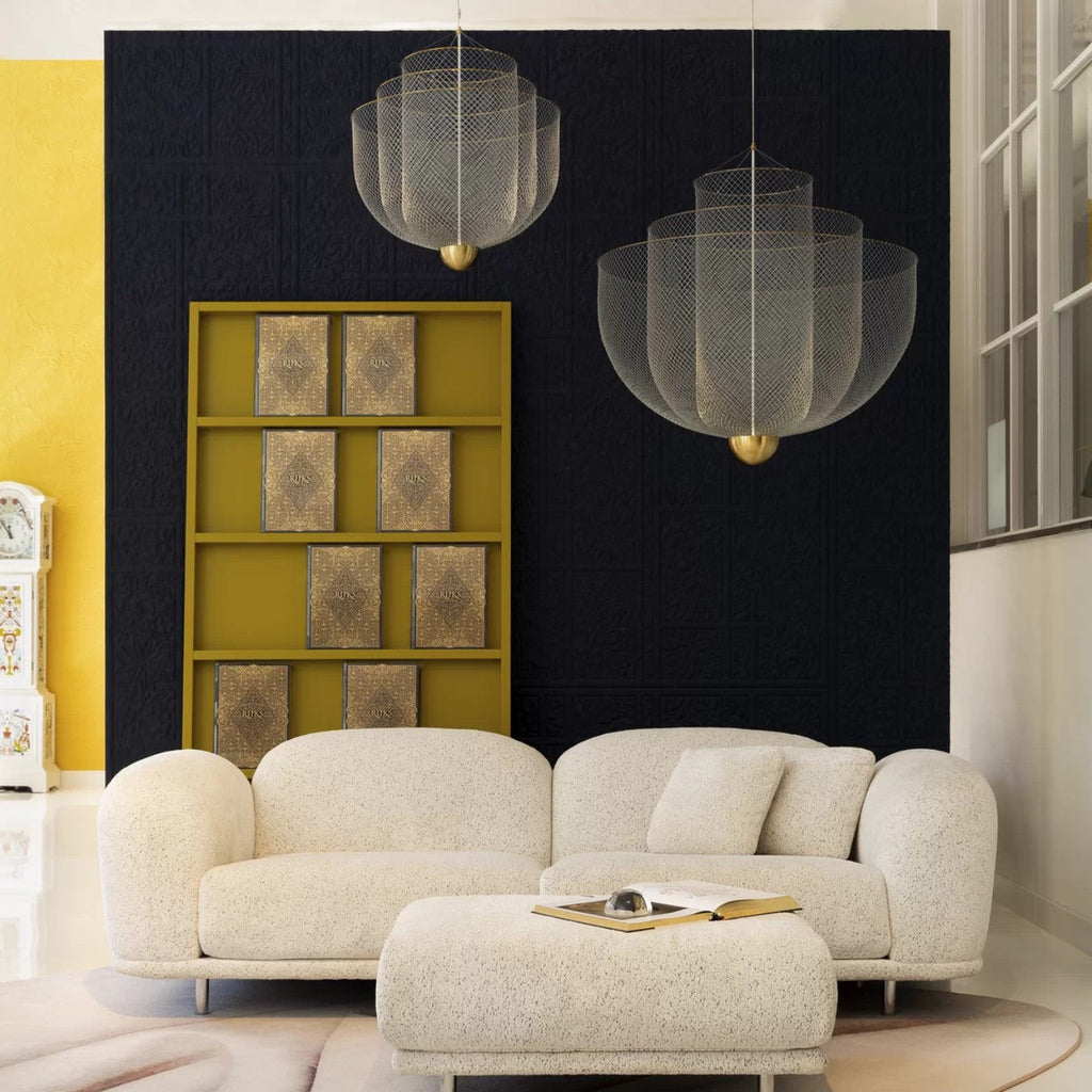 Two Clérachic wire-mesh chandeliers hang against a dark blue wall above a white sofa and ottoman, with a mustard shelf nearby.