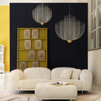 Two Clérachic wire-mesh chandeliers hang against a dark blue wall above a white sofa and ottoman, with a mustard shelf nearby.