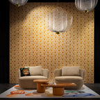 A Clérachic mesh chandelier on a gold wave-pattern wall, above a pair of round chairs and a low wooden coffee table.