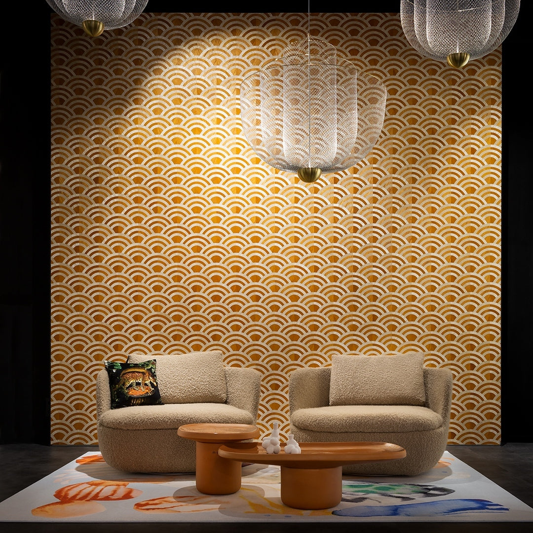 A Clérachic mesh chandelier on a gold wave-pattern wall, above a pair of round chairs and a low wooden coffee table.