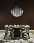 Clérachic silver wire-mesh chandelier above a dark round table with six upholstered chairs, on a patterned rug against a dark brown wall.