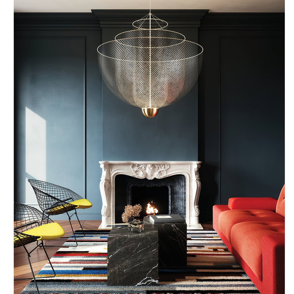 Clérachic wire-mesh chandelier in front of a dark blue panelled wall with a white fireplace, a black marble table and a red sofa.