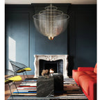 Clérachic wire-mesh chandelier in front of a dark blue panelled wall with a white fireplace, a black marble table and a red sofa.