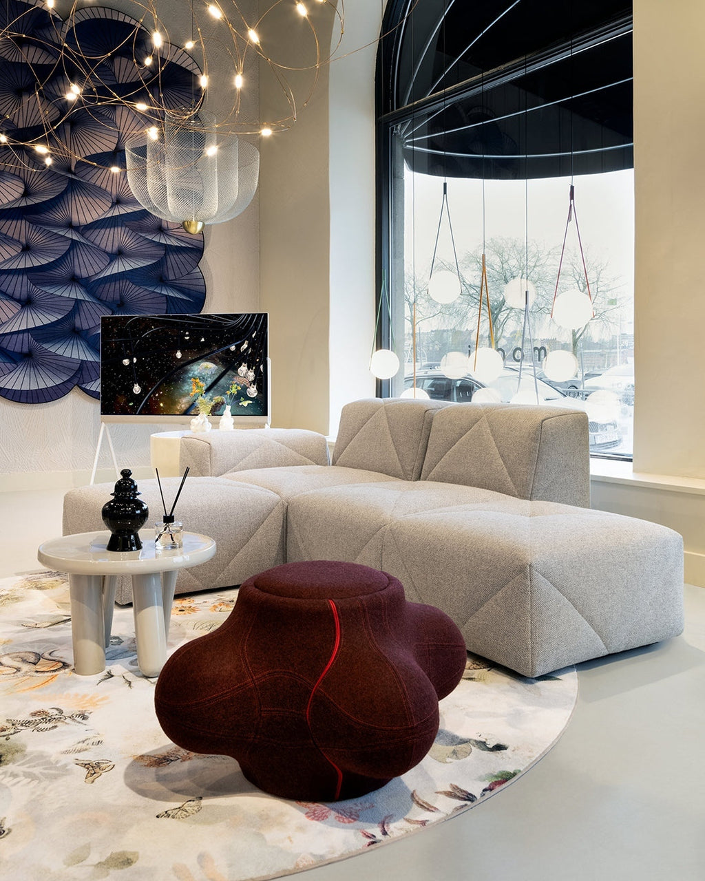 Clérachic wire-mesh chandelier in a bright showroom with a cream corner sofa, a round rug and a small side table.