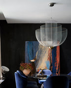 Clérachic wire-mesh chandelier in a dark room with a large abstract painting, blue velvet chairs and a small plant.