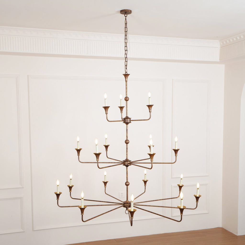 Clérachic's Wisp Grande chandelier hangs lit above a wood floor, its bulbs glowing warm in a paneled room.