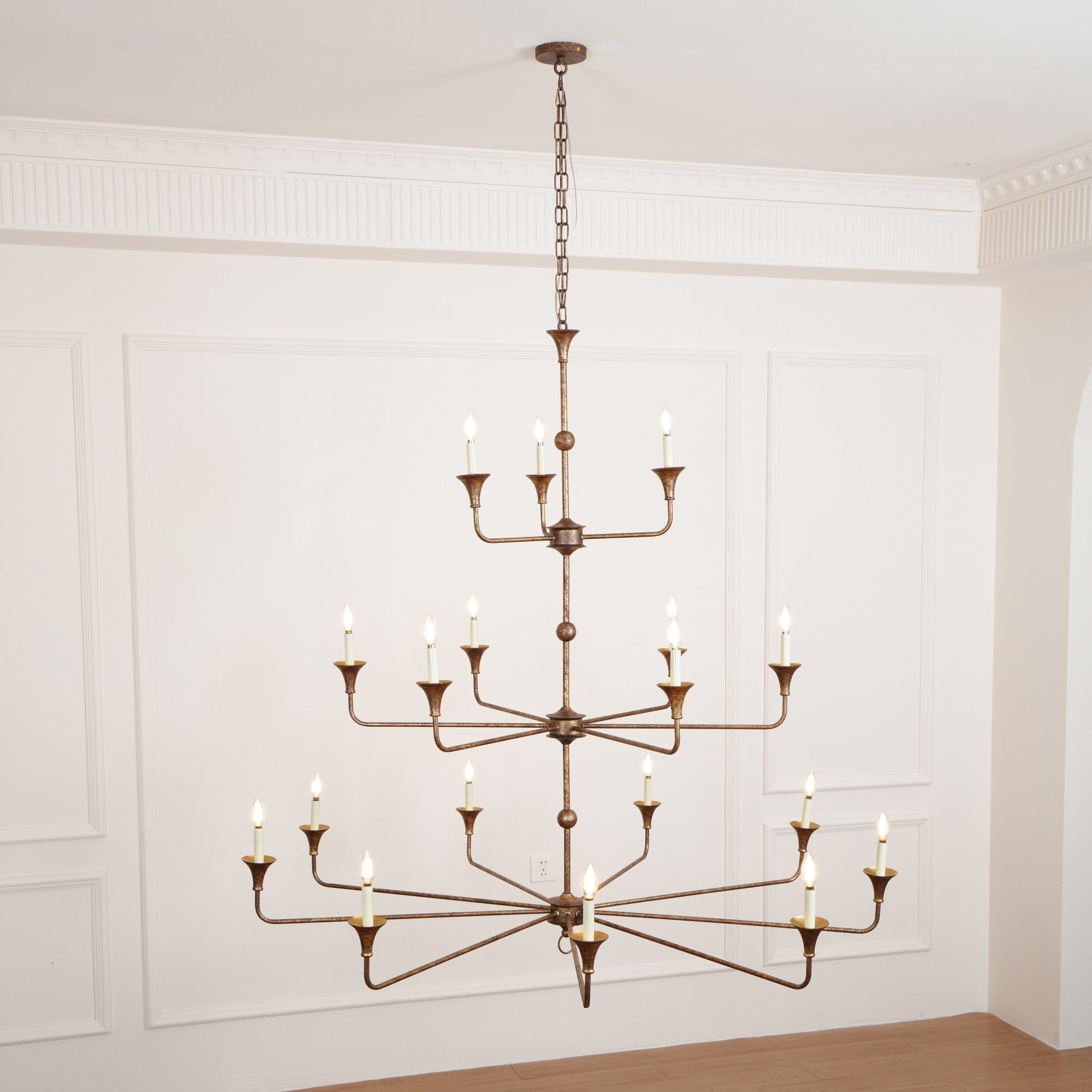 Clérachic's Wisp Grande chandelier hangs lit above a wood floor, its bulbs glowing warm in a paneled room.