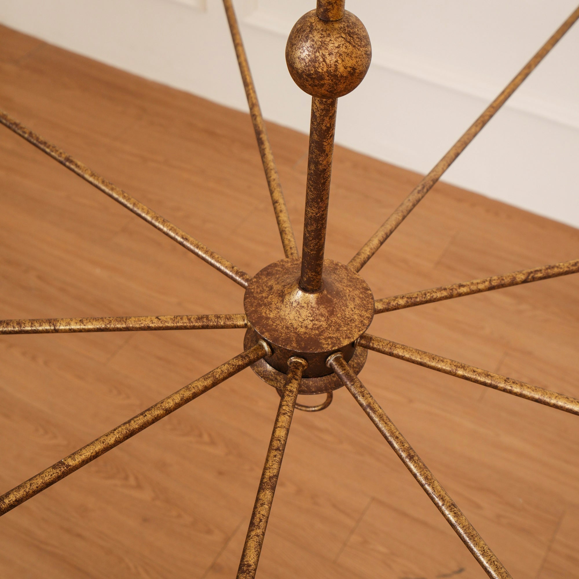 The Clérachic Wisp Grande chandelier's bronze center hub photographed close on a wood floor, arms fanning out.