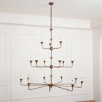 Clérachic's Wisp Grande chandelier hangs lit on a long chain drop, bronze tiers centered on a paneled wall.