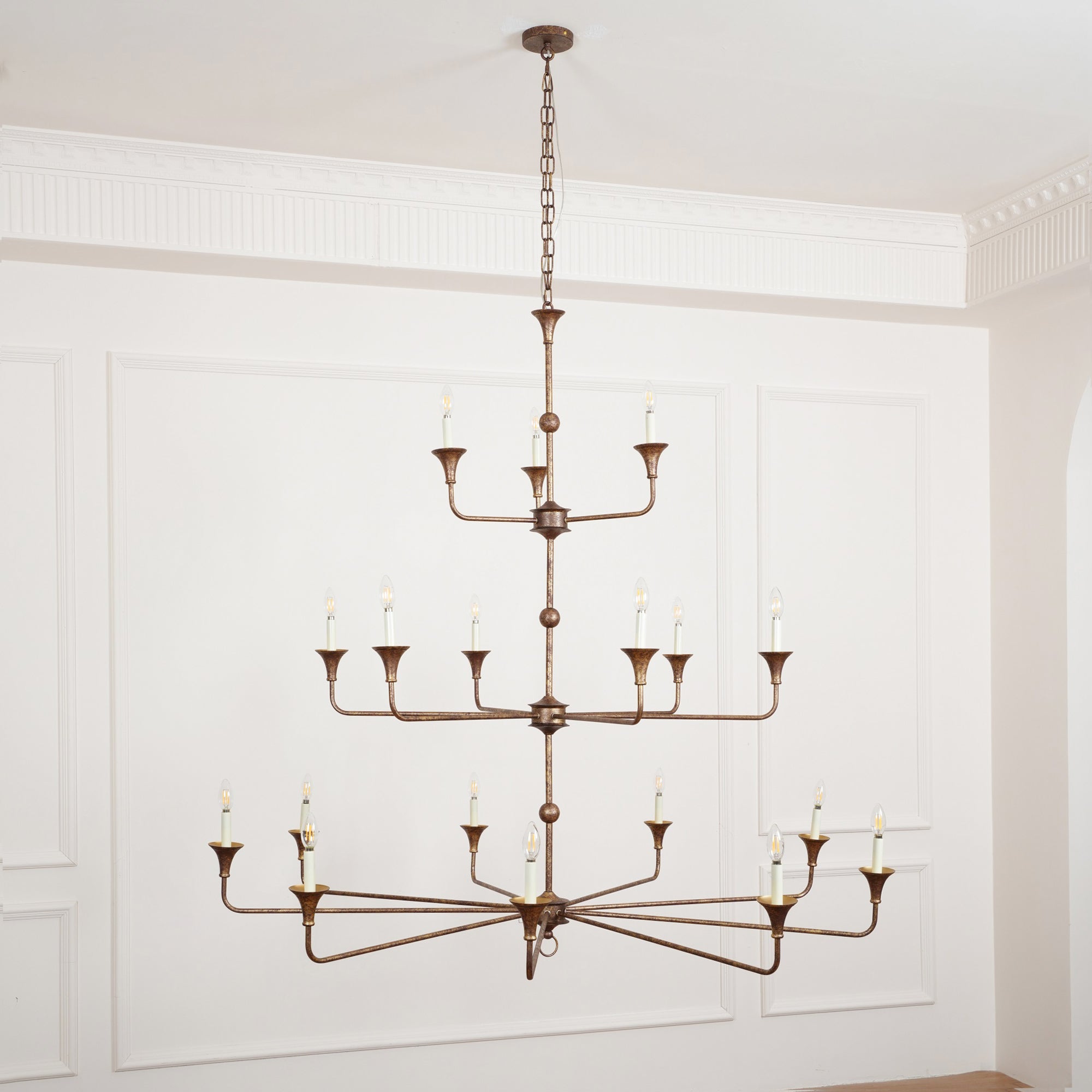Clérachic's Wisp Grande chandelier hangs lit on a long chain drop, bronze tiers centered on a paneled wall.