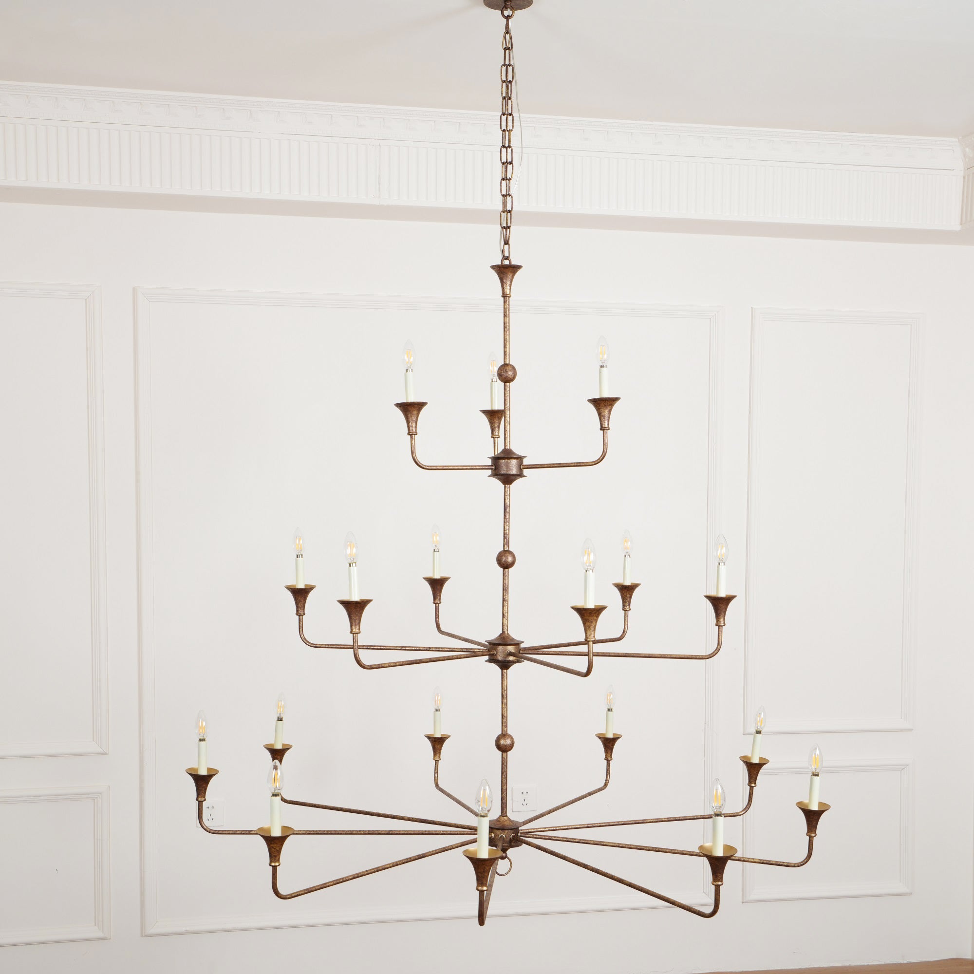 The Clérachic Wisp Grande chandelier glows at a slight angle, three bronze tiers spreading warm light indoors.
