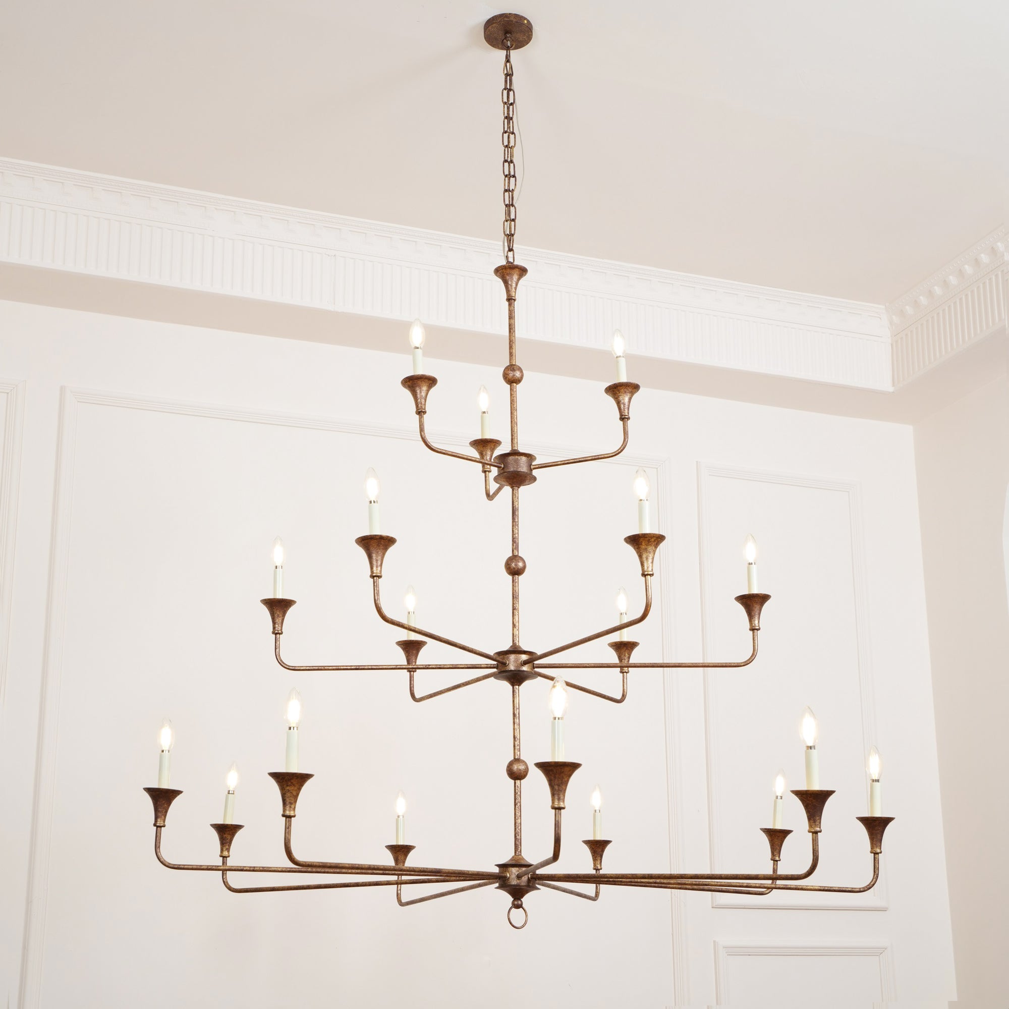 The Clérachic Wisp Grande chandelier hangs high on its chain, bronze arms glowing across three tiers.