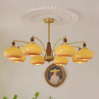Clérachic Wood and Brass Chandelier in caramel, eight shades lit above a gilt-framed portrait on a pale wall.