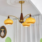 Clérachic Wood and Brass Chandelier in caramel, three shades lit in a corner beside sheer white curtains.