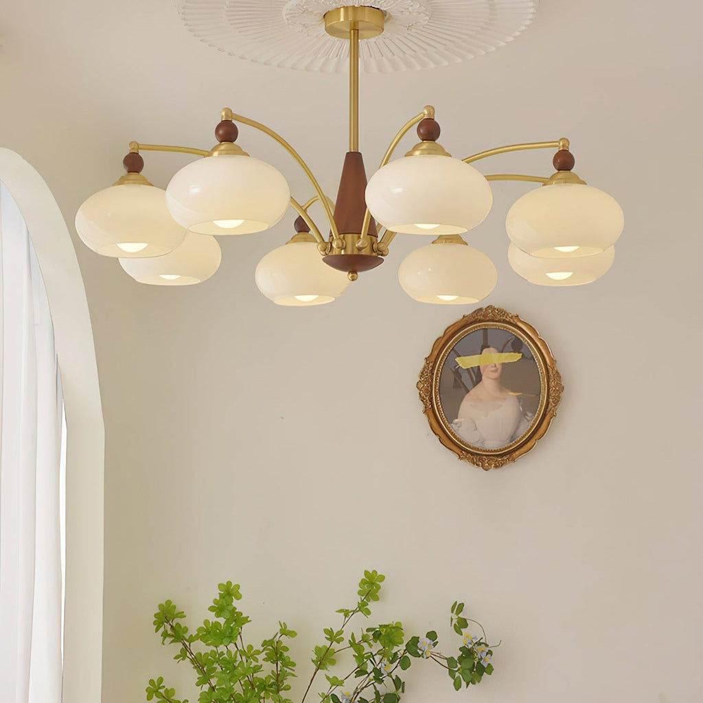 Clérachic Wood and Brass Chandelier in white, its eight shades lit in a bright room with sheer curtains.