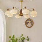 Clérachic Wood and Brass Chandelier in white, its eight shades lit in a bright room with sheer curtains.