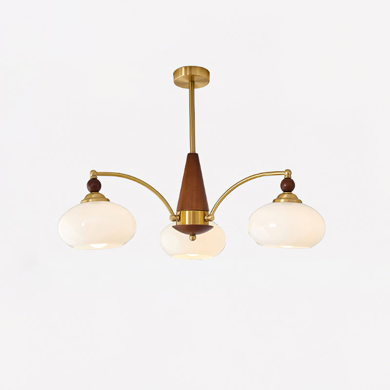 Clérachic three-light Wood and Brass Chandelier in milk glass, ovoid shades glowing on a grey studio wall.