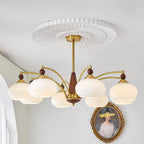 Clérachic eight-light Wood and Brass Chandelier in white glass, lit beside an arched window and gilt frame.