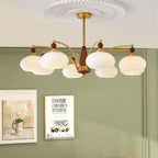 Clérachic eight-light Wood and Brass Chandelier in white glass, hung before a sage wall and framed prints.