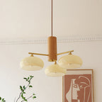Clérachic wood and brass chandelier with three beige persimmon glass shades, unlit above a living room wall of art prints.