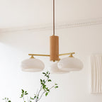 Three white persimmon glass shades on the Clérachic wood and brass chandelier, unlit against a pale wall and moulded cornice.