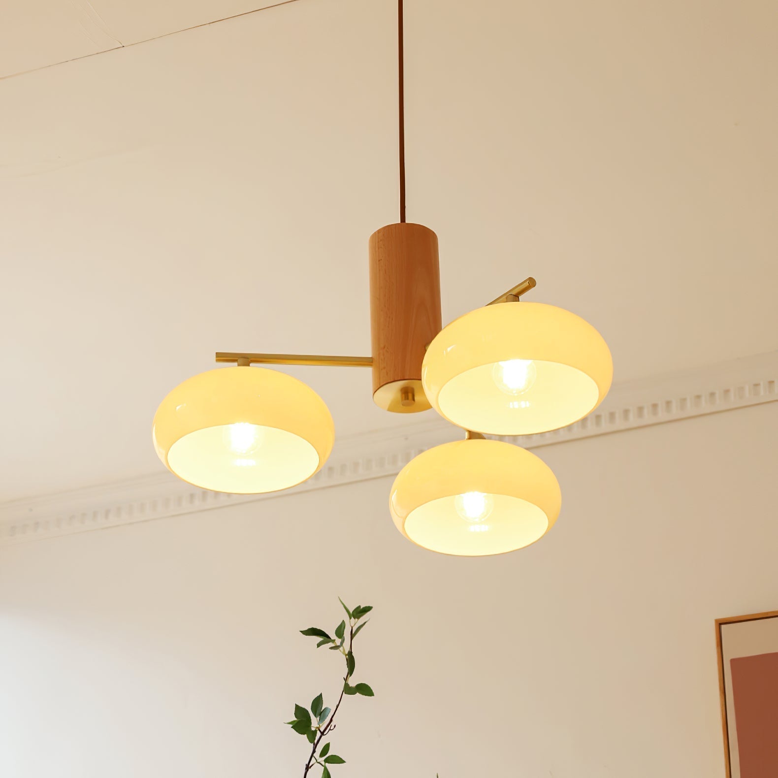 Lit close-up of the Clérachic three-light chandelier, bulbs glowing behind the open discs of the beige glass shades.