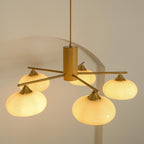 The Clérachic five-light chandelier lit in white glass, brass cone fitters and long rods staggered at two heights.