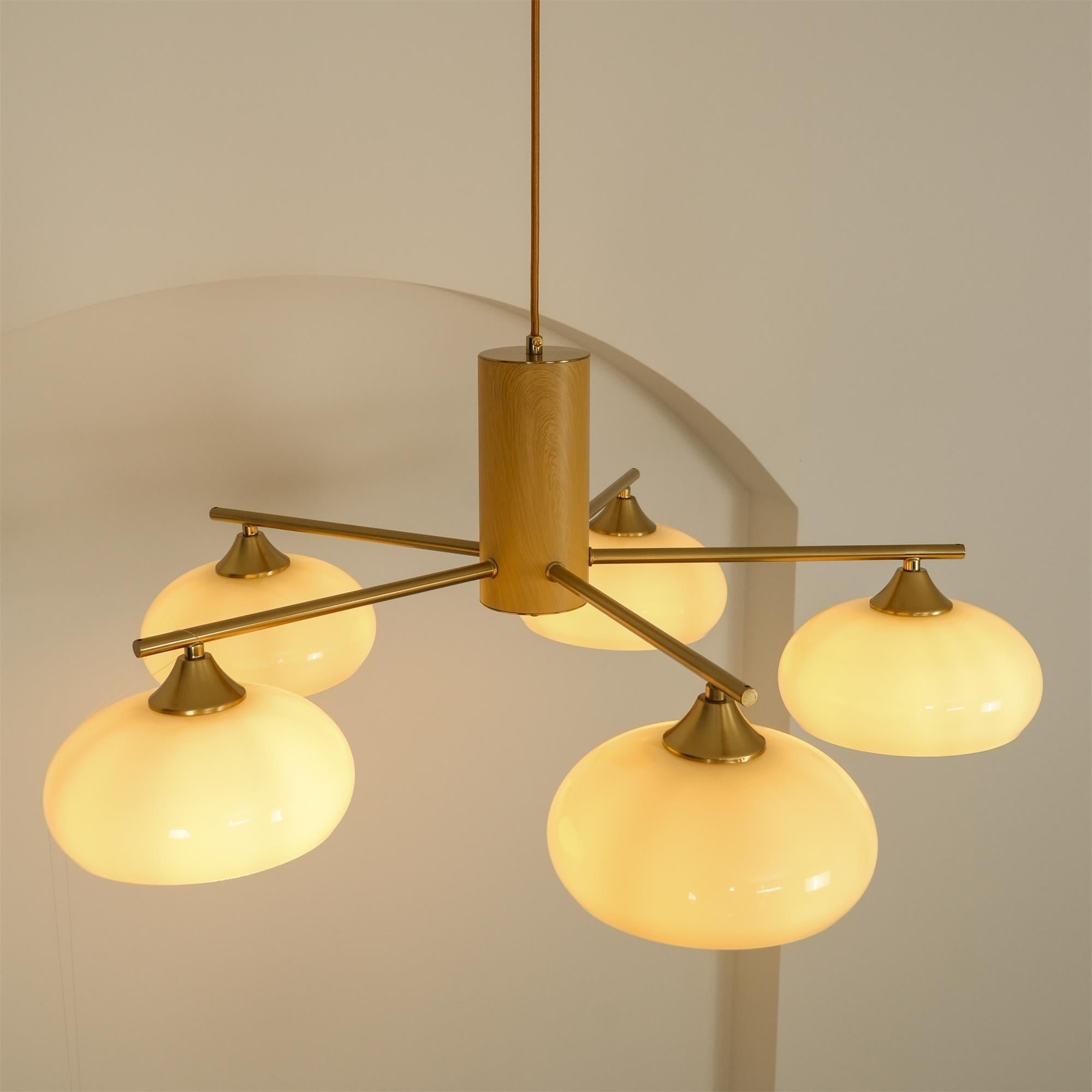 The Clérachic five-light chandelier lit in white glass, brass cone fitters and long rods staggered at two heights.