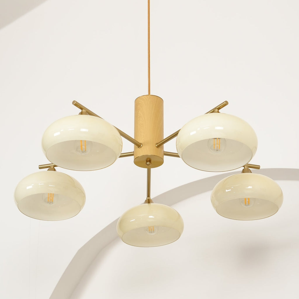 Clear filament bulbs glow through the beige glass of the Clérachic five-light chandelier in a studio corner.